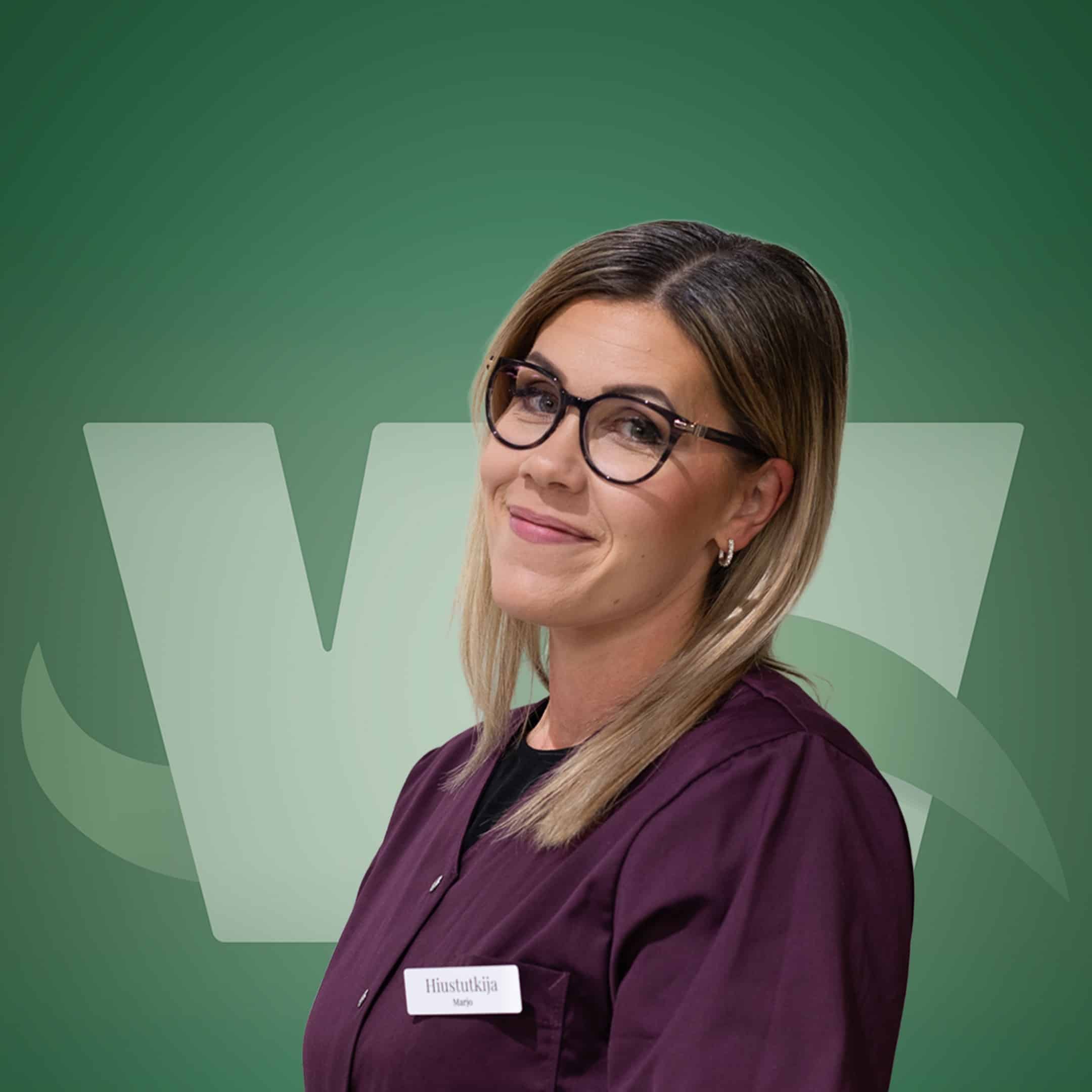 Portrait of a person wearing glasses in a burgundy top against a green backdrop, with a name badge reading 'Hiustutkija' (likely 'Marjo').